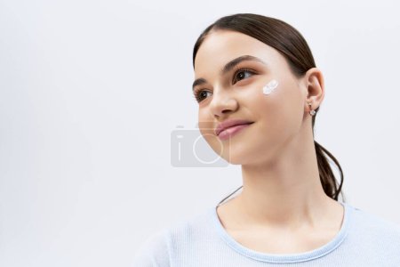A gorgeous brunette teenage girl applying white face cream to her cheek, exuding youthful beauty.