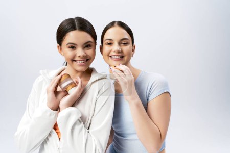 Two pretty brunette teenage girls with cream jar on a grey background.