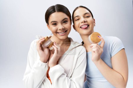 Téléchargez les photos : Deux adolescentes jolies et brunes en tenue de sport posent tout en tenant de la crème dans un studio sur fond gris. - en image libre de droit