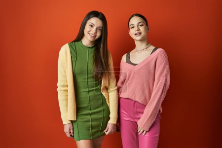 two pretty teenage girls in casual attire standing together on orange background