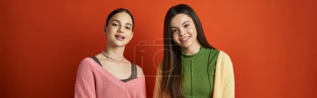 Téléchargez les photos : Deux adolescentes jolies et brunes debout ensemble devant un mur rouge vibrant, mettant en valeur l'amitié et l'unité. - en image libre de droit