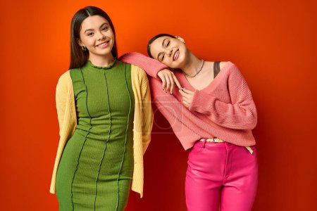 Téléchargez les photos : Deux jolies adolescentes brunes en tenue décontractée se tiennent côte à côte sur un fond de studio orange. - en image libre de droit