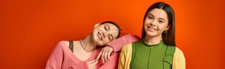 Téléchargez les photos : Deux jolies adolescentes brunes en tenue décontractée se tiennent étroitement ensemble sur un fond orange vif dans un studio. - en image libre de droit