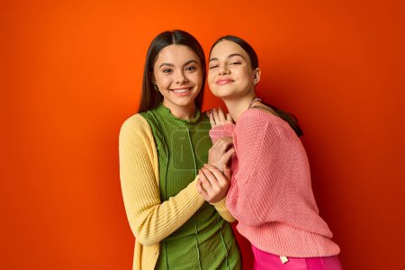 Zwei hübsche, lässige brünette Freundinnen stehen vor einer lebhaften orangefarbenen Wand und strahlen Vertrauen und Freundschaft aus.