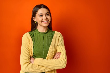 Photo for A brunette woman standing with arms crossed against an orange backdrop exuding confidence and poise. - Royalty Free Image