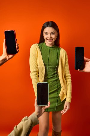 Ein brünettes Teenager-Mädchen in einem grünen Kleid in der Nähe von Mobiltelefonen, das Multitasking und moderne Konnektivität präsentiert.