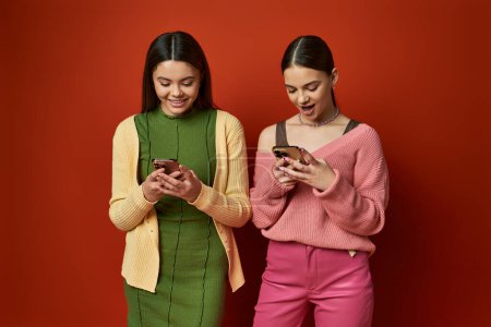 Zwei hübsche, brünette Teenager-Mädchen stehen zusammen, in ihre Handys vertieft und ignorieren ihre Umgebung.