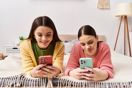 Téléchargez les photos : Deux adolescentes en tenue décontractée se détendent sur un lit, absorbées dans leurs téléphones cellulaires. - en image libre de droit