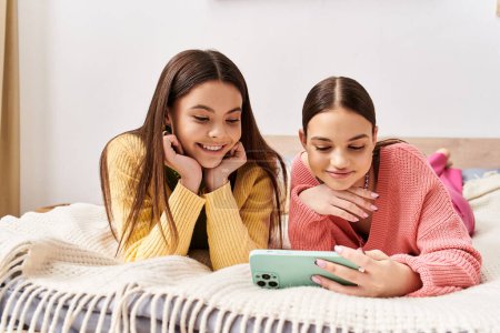 Photo for Two teenage girls, in casual attire, lay on a bed absorbed in a screen, sharing moments of joy and discovery. - Royalty Free Image