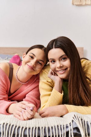 Téléchargez les photos : Deux belles adolescentes en vêtements décontractés se prélassant ensemble sur un lit, profitant mutuellement de la compagnie dans un cadre confortable. - en image libre de droit