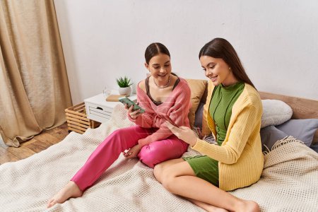 Foto de Dos adolescentes se sientan en una cama, absortas en un teléfono celular. - Imagen libre de derechos