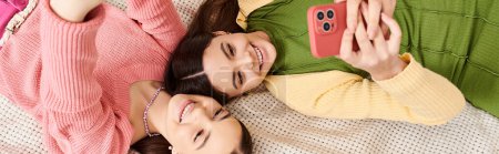 Téléchargez les photos : Deux jeunes femmes élégantes en vêtements décontractés, paisiblement côte à côte sur un lit confortable à la maison. - en image libre de droit