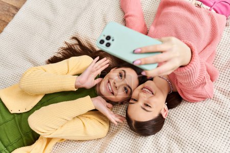 Zwei junge Frauen kleideten sich lässig und teilten einen Moment des Lachens, als sie in ein Handy vertieft auf einem Bett lagen.