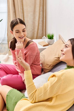 Two pretty teenage girls in casual attire, female friends, sit on a bed, engrossed in a heartfelt discussion.