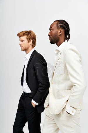 Dos hombres guapos multiculturales en trajes elegantes caminando juntos.