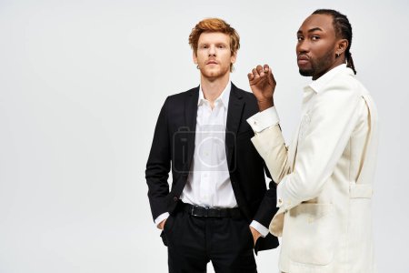 Zwei gutaussehende, multikulturelle Männer in eleganter Kleidung stehen zusammen vor weißem Hintergrund.