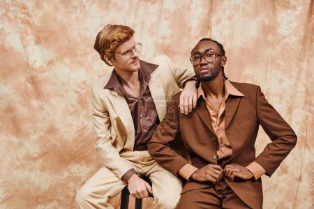 Zwei gutaussehende multikulturelle Männer in eleganter Kleidung sitzen eng beieinander.