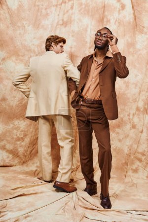 Foto de Dos guapos hombres multiculturales en elegante estilo elegante posan uno al lado del otro frente a una pared. - Imagen libre de derechos