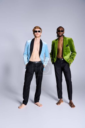 Téléchargez les photos : Deux beaux hommes multiculturels avec style élégant dapper stand côte à côte devant un fond gris. - en image libre de droit