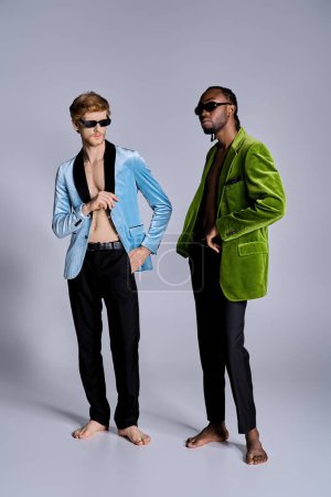 Foto de Dos hombres multiculturales en elegante atuendo se paran uno al lado del otro frente a un telón de fondo gris. - Imagen libre de derechos