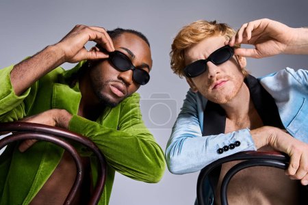 Zwei multikulturelle Männer in eleganter Kleidung und Sonnenbrille posieren für einen Schnappschuss.