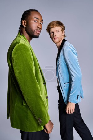 Dos elegantes hombres multiculturales posando con estilo frente a un fondo gris.