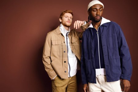 Téléchargez les photos : Deux hommes multiculturels élégants debout ensemble devant un mur brun. - en image libre de droit