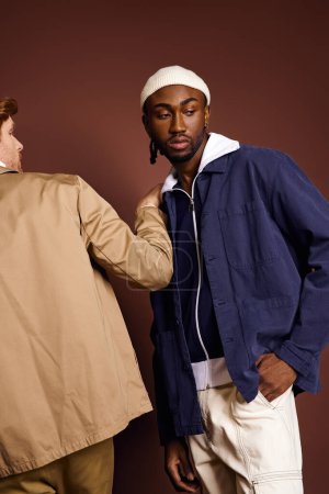 Foto de Dos hombres multiculturales vestidos con estilo se unen sobre un fondo marrón. - Imagen libre de derechos