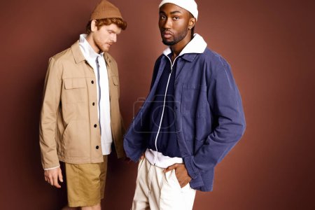 Foto de Dos hombres multiculturales con estilo de pie frente a una pared marrón. - Imagen libre de derechos
