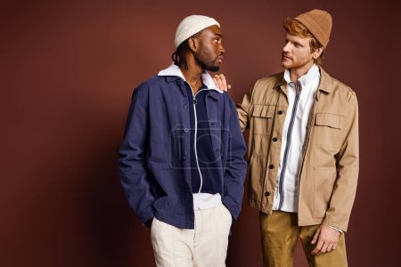 Foto de Dos elegantes hombres multiculturales posan elegantemente frente a una pared marrón. - Imagen libre de derechos