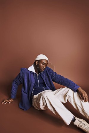 Stilvoller afroamerikanischer Mann sitzt mit Hut auf dem Boden.