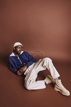 A young African American man seated on the ground, wearing a stylish hat.