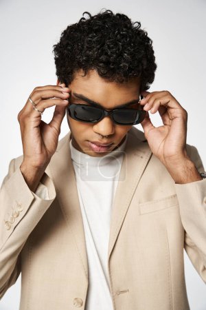 Young man exudes style in tan suit and sunglasses.