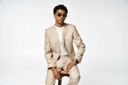 Schöner afroamerikanischer Mann mit stylischer Sonnenbrille sitzt auf einem Hocker.