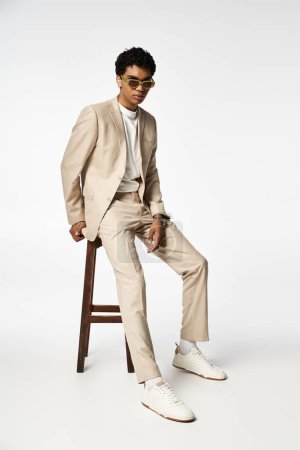 Hombre afroamericano guapo en traje de bronceado sentado en el taburete con gafas de sol elegantes.