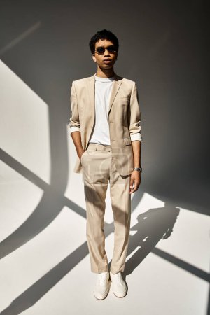 Handsome African American man in beige suit and stylish sunglasses standing in front of white wall.