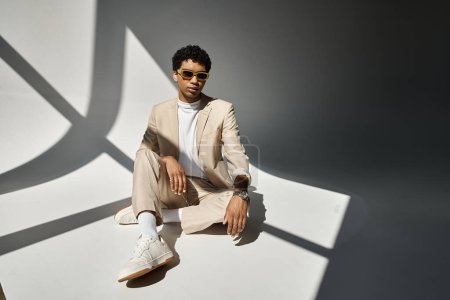 Photo for African American man in beige suit sitting comfortably on the floor, wearing stylish sunglasses. - Royalty Free Image