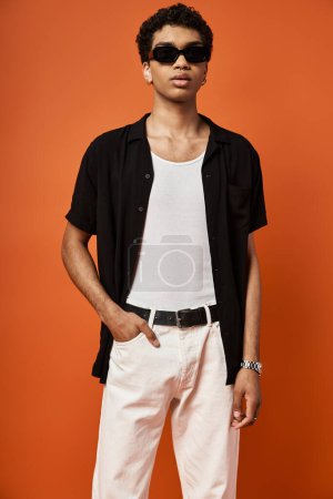 Foto de Hombre afroamericano guapo en pantalones blancos y camisa negra con gafas de sol elegantes. - Imagen libre de derechos