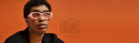 Schöner afroamerikanischer Mann mit pinkfarbener Brille vor orangefarbenem Hintergrund.