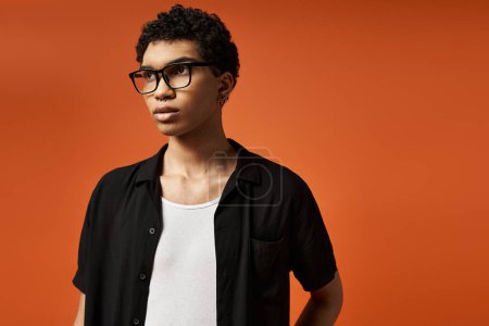 Handsome African American man in stylish glasses stands confidently against vivid orange backdrop.