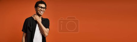 Photo for Handsome African American man in stylish glasses posing against a bold orange background. - Royalty Free Image