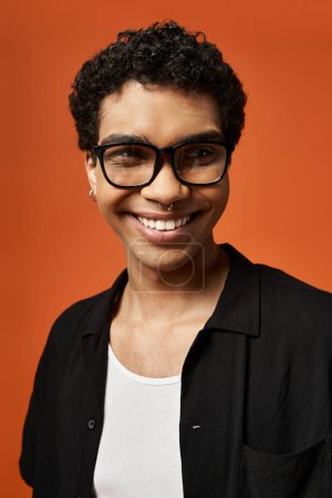 Stylish African American man in glasses smiles brightly on vibrant orange background.