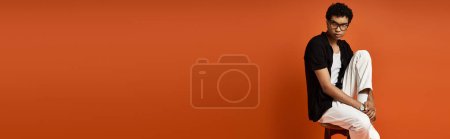 Photo for African American man with sunglasses sitting on a chair in front of orange wall. - Royalty Free Image