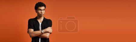Stylish African American man with arms folded in front of bold orange backdrop.