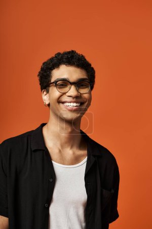 Téléchargez les photos : Bel homme avec des lunettes de soleil élégantes souriant sur fond orange audacieux. - en image libre de droit