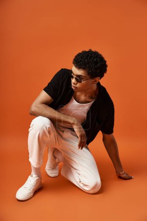 Handsome African American man in stylish sunglasses crouching on orange background.