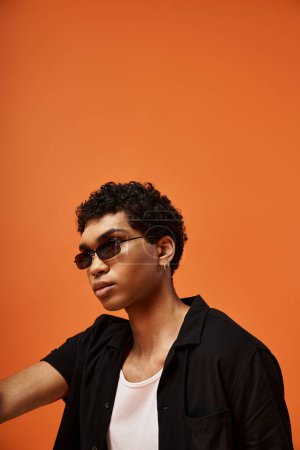 Handsome young man in sunglasses against bright orange backdrop.