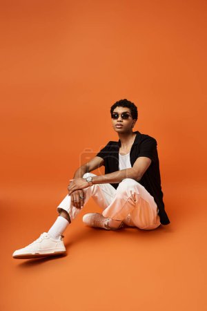 Stylish African American man sitting on bright orange background with white sneakers.