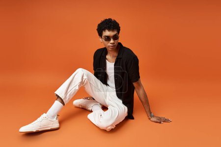 African American man posing with sunglasses against bold orange backdrop.