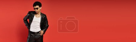 Téléchargez les photos : Beau homme en veste en cuir et lunettes de soleil frappant une pose sur fond rouge vif. - en image libre de droit